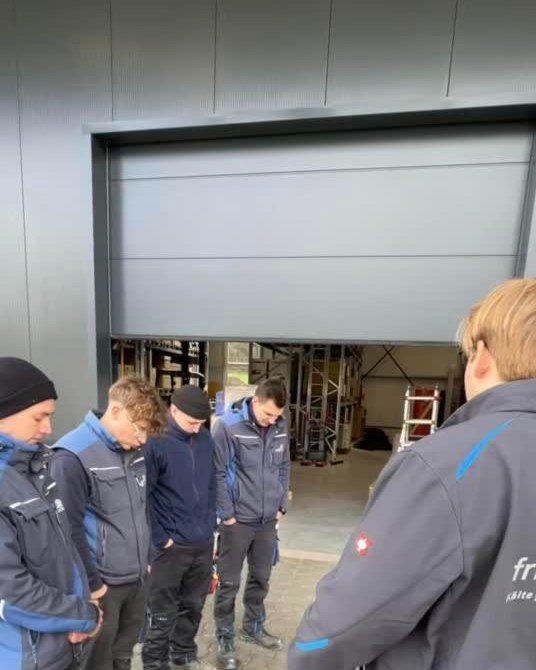 Trend-Video bei frigoclim: Mitarbeiter in Arbeitsjacken stehen mit gesenktem Kopf vor einer Hallentür